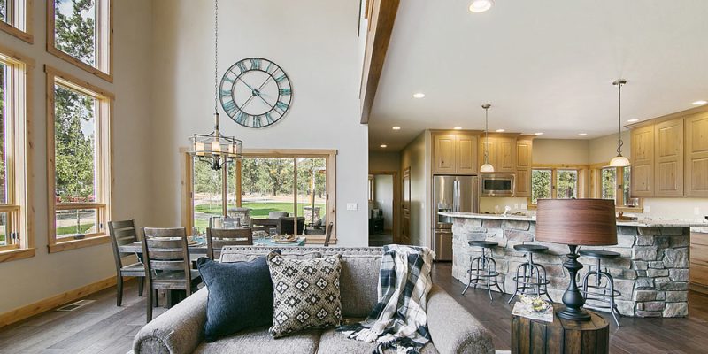 A rustic living room with high ceilings, large windows, and a stone kitchen bar, blending modern and traditional design elements for a welcoming space.