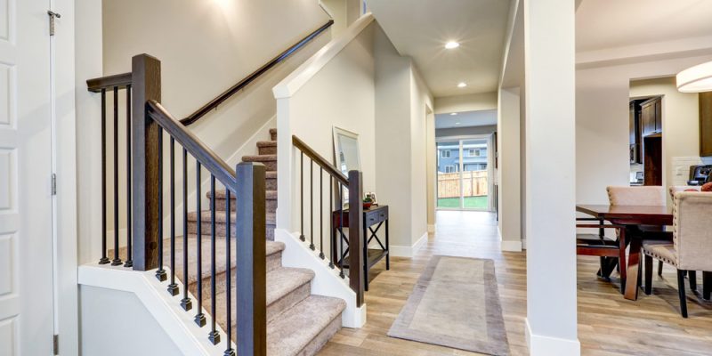 A sophisticated entryway featuring a modern staircase with wooden steps and dark railings, leading to an elegantly lit hallway.