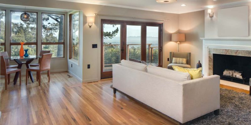 A warm and inviting living room with a modern fireplace, comfortable seating, and large windows offering scenic views of the outdoors, complemented by hardwood flooring.