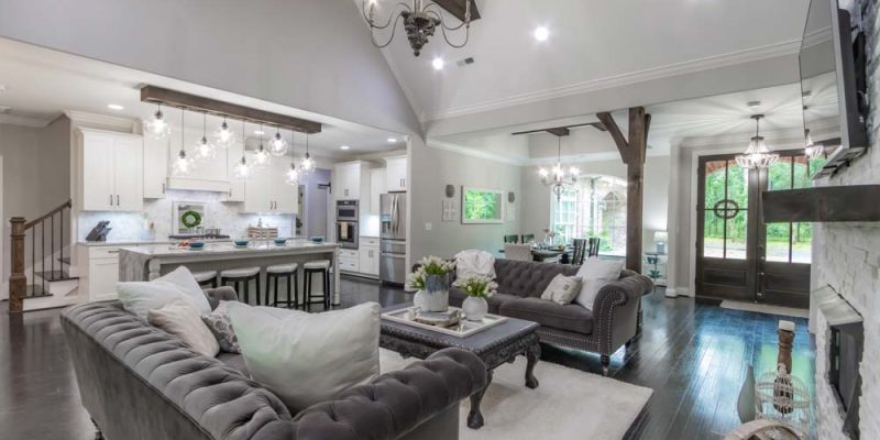 A luxurious living room with high ceilings, rustic wooden beams, a large stone fireplace, and elegant chandeliers, creating a perfect blend of modern and classic design.