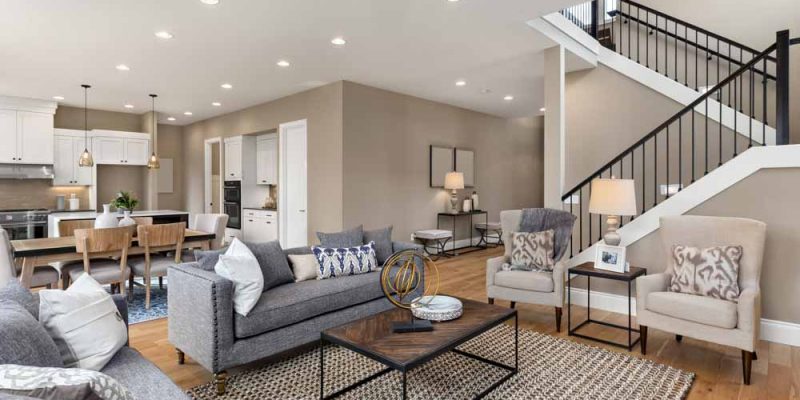 A spacious open-concept living area with a modern kitchen, featuring neutral-toned furniture, a dining area, and a stylish staircase leading to the upper level.