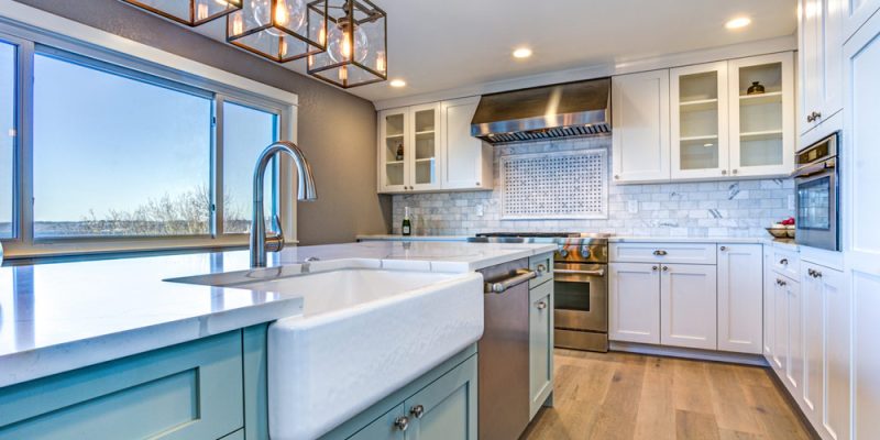 Modern kitchen with white cabinetry, a large farmhouse sink, and stylish blue accents under natural light, demonstrating expert kitchen remodeling.
