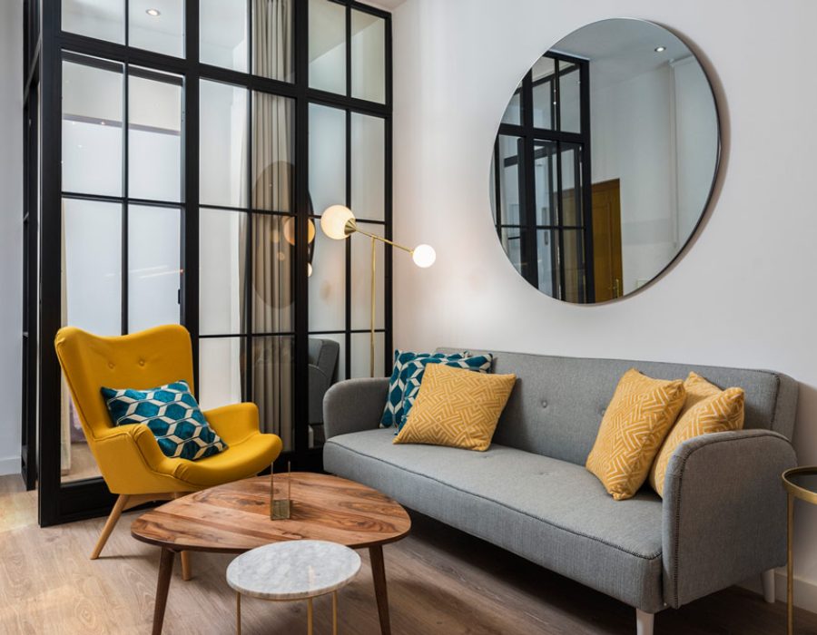 Chic living room with black framed glass doors, a yellow accent chair, and modern decor elements, showcasing stylish interior remodeling.