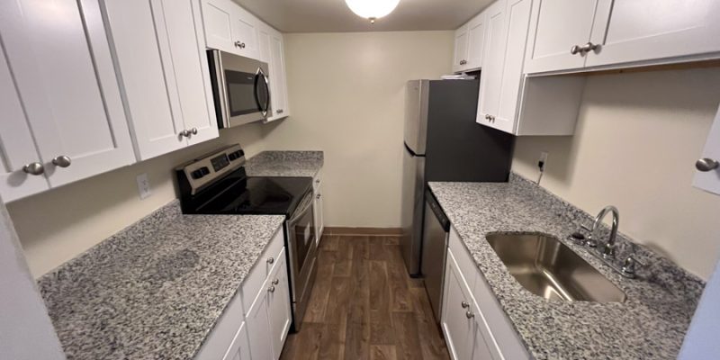 A newly remodeled kitchen featuring white cabinets, gray granite countertops, and stainless steel appliances, offering a contemporary look and efficient use of space.